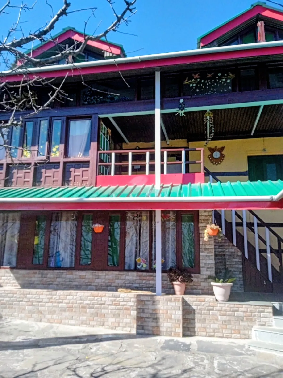 The family home in Dobhi, Kullu — wooden balconies, a green tin roof, and potted plants along the front of the house